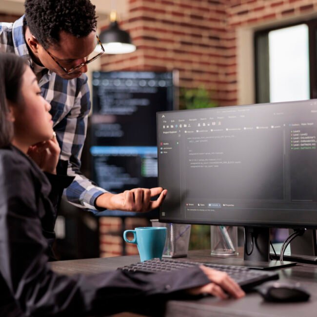 Diverse programmers discussing about html code compiling discovers errors, standing in front of multiple screens in startup office. Software developers working on server interface development.